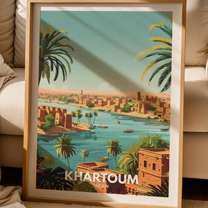 May include: A framed travel poster featuring a stylised illustration of the city of Khartoum, Sudan. The artwork depicts a river flowing through a desert landscape with palm trees, buildings, and small boats. The text KHARTOUM SUDAN is at the bottom.
