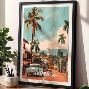 May include: A framed art print of Kampala, Uganda, featuring a vintage car on a road lined with buildings and palm trees. The artwork has a retro travel poster style with a color palette of blues, oranges, and greens. The word "Kampala" is prominently displayed.
