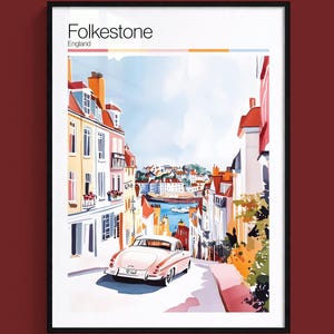 May include: A framed art print titled Folkestone England featuring a street scene with colourful buildings, a vintage white car driving down a hill toward the sea, and a clear blue sky. The print includes a colour palette bar at the top.
