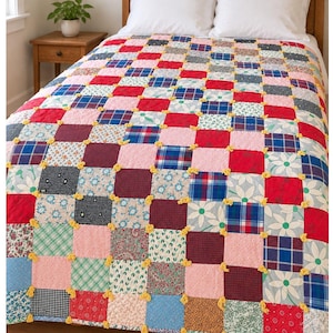 May include: A patchwork quilt featuring a grid of square fabric patches in various patterns including red, blue, and green plaids, floral prints, and white daisy motifs. The squares are joined by small, bright yellow yarn ties at each corner.