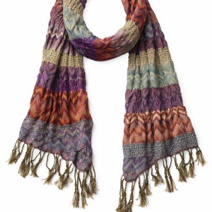 May include: A long scarf featuring a multi-colored chevron pattern in shades of purple, orange, blue, and tan. The fabric has a crinkled texture with horizontal bands of varying knit patterns and finishes with long, thin, olive-colored fringe tassels.