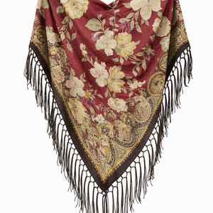 May include: A burgundy shawl with a floral pattern featuring large cream-colored flowers and green leaves. The shawl has a dark brown border with a paisley design and black fringe.