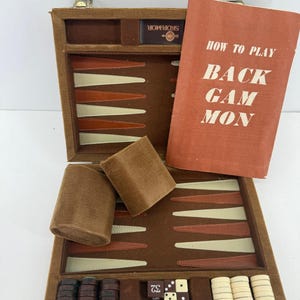 May include: A brown corduroy backgammon set in a carrying case with a board featuring alternating cream and brown triangles. Includes two brown dice cups, a set of brown and cream checkers, a doubling cube with the number 32, and a manual.