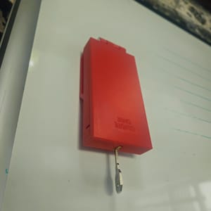 Puede incluir: Una funda roja brillante para mando a distancia con la inscripción "REMOTE CASE" impresa en el lateral. Una pequeña llave plateada cuelga de la parte inferior. La funda es rectangular y parece ser de plástico.