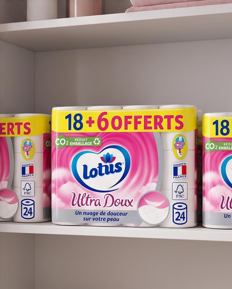 以下が含まれることがあります： 棚に積み重ねられた、Lotus Ultra Douxトイレットペーパーの複数のパッケージ。パッケージはピンクと白で、ブランド名と製品の説明がフランス語で書かれています。パッケージには「18 + 6 OFFERTS」と書かれた黄色のバナーが付いています。