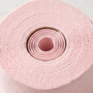 Puede incluir: Primer plano de un rollo de papel de cocina rosa. El papel est&aacute; enrollado alrededor de un n&uacute;cleo central de cart&oacute;n. La superficie del papel tiene una apariencia texturizada y el color es un rosa suave y uniforme.
