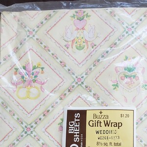 Könnte beinhalten: Hochzeitsgeschenkpapier in einer transparenten Kunststoffverpackung. Das Papier hat ein sich wiederholendes Muster aus Herzen, Tauben, Blumen und Eheringen auf hellgelbem Hintergrund. Das Etikett lautet "Buzza Gift Wrap WEDDING". Jedes Blatt misst 50.8 cm x 76.2 cm.