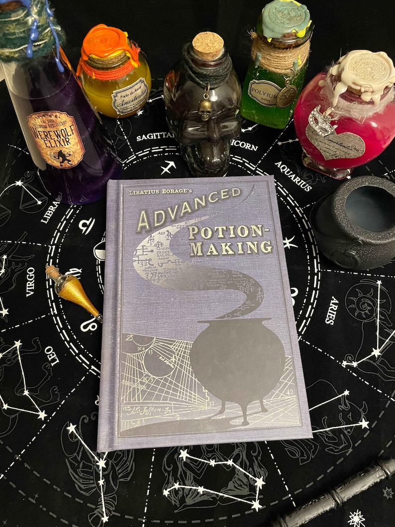 Op de afbeelding: Een verzameling benodigdheden voor het maken van drankjes, waaronder een boek getiteld "Advanced Potion-Making" en diverse drankflessen. De flessen zijn gevuld met kleurrijke vloeistoffen en versierd met etiketten en decoratieve elementen. Een zwarte ketel en een toverstaf zijn ook aanwezig.