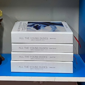 May include: Four white books stacked on top of each other. The book titles read "ALL THE YOUNG DUDES" with "SIRIUS PERSPECTIVE" below. The books are labeled "Book One" through "Book Four". The top book has a blue and white abstract design.