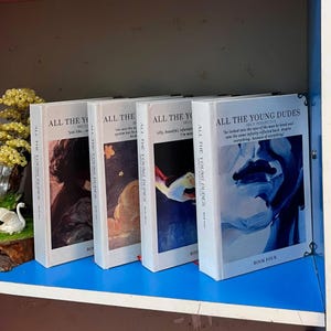 May include: Four hardcover books titled "ALL THE YOUNG DUDES" are displayed. Each book has a white cover with text and abstract art. The spines also have the title. Book Four has a quote and the words "BOOK FOUR" at the bottom.