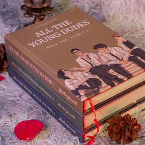 Puede incluir: Una pila de cuatro libros con el t&iacute;tulo "ALL THE YOUNG DUDES". El libro superior es marr&oacute;n con una ilustraci&oacute;n de j&oacute;venes. Los otros libros son de color verde oscuro y azul. Cintas rojas marcan las p&aacute;ginas.