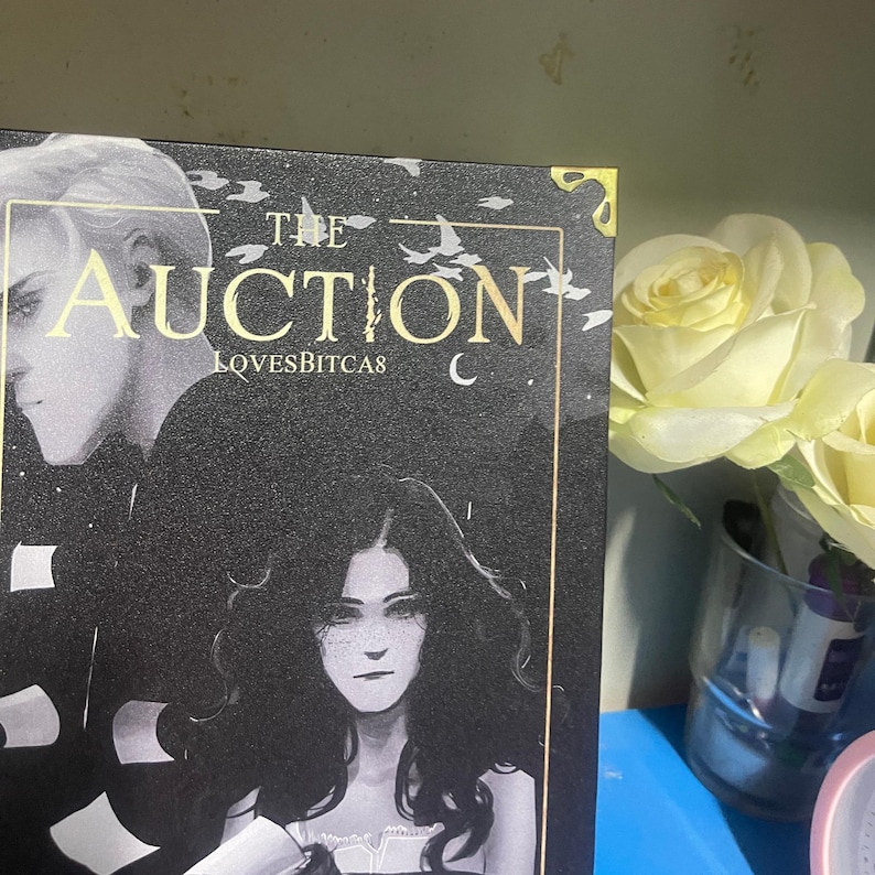 Puede incluir: Portada de libro con el t&iacute;tulo "The Auction" en letras doradas. La portada presenta un fondo oscuro con ilustraciones de dos personas. El texto "LOVESBITCAS" est&aacute; debajo del t&iacute;tulo. Un ramo de rosas amarillas est&aacute; en el fondo.