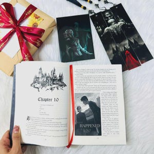 May include: An open book with Chapter 10 displayed, featuring a castle illustration. A red ribbon bookmark is visible. Beside it are two art prints and a wrapped gift with a red ribbon.