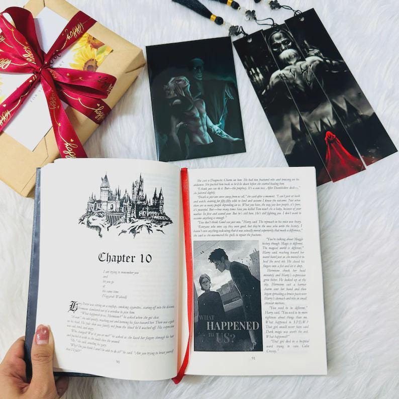 May include: An open book with Chapter 10 displayed, featuring a castle illustration. A red ribbon bookmark is visible. Beside it are two art prints and a wrapped gift with a red ribbon.
