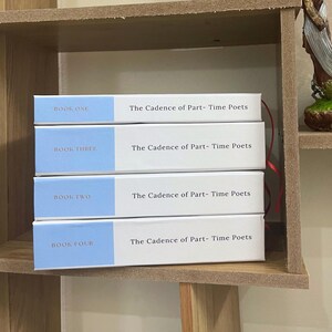 May include: Four books titled "The Cadence of Part-Time Poets" are stacked on a wooden shelf. Each book has a white cover with a light blue band at the top, displaying "BOOK ONE", "BOOK THREE", "BOOK TWO", and "BOOK FOUR".
