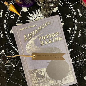 Op de afbeelding: Een lavendelkleurig boek getiteld "Advanced Potion-Making" van Libatius Borage, met een bladwijzer met de tekst "After all this time? -Always." Het boek heeft zilverfolie accenten en een vogel silhouet. De achtergrond bevat drankflessen en een schedel.