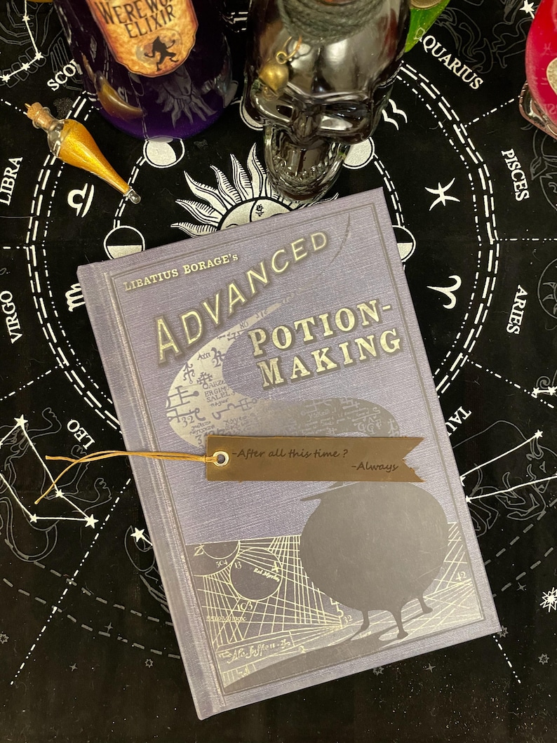 Op de afbeelding: Een lavendelkleurig boek getiteld "Advanced Potion-Making" van Libatius Borage, met een bladwijzer met de tekst "After all this time? -Always." Het boek heeft zilverfolie accenten en een vogel silhouet. De achtergrond bevat drankflessen en een schedel.