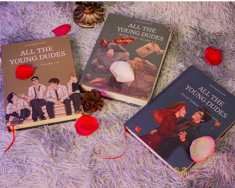 Puede incluir: Tres libros titulados "All The Young Dudes" se muestran sobre una superficie esponjosa, con p&eacute;talos de rosa rojos esparcidos. Las portadas de los libros presentan ilustraciones de personajes y el texto "Years 1-4", "Book Two: Years 1-7" y "Book Three: Til The End".