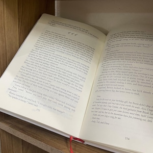 May include: Open book with text on the pages, a red ribbon bookmark, and a wooden surface. The text is in English. The book is open to pages 193 and 194.