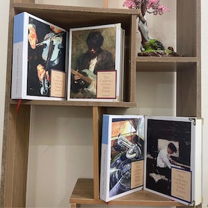 May include: A wooden bookshelf displays several books titled "The Cadence of Part-Time Poets." The book covers feature vintage-style illustrations of musicians playing instruments. The books have white spines with blue accents and gold corner protectors.
