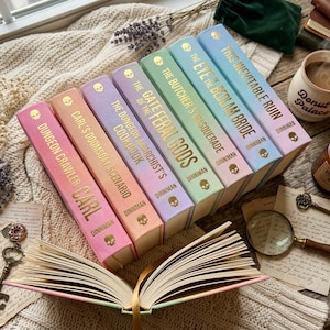 May include: A selection of fantasy novels with pastel-coloured spines, gold lettering, and skull icons. An open book, a lit candle, a mug of coffee, and a magnifying glass are also visible, creating a cosy, inviting atmosphere.