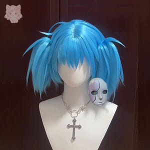May include: A bright blue wig styled with two side pigtails and bangs, displayed on a white mannequin head. The mannequin wears a silver-toned chain necklace featuring a large cross pendant and a small, pale mask with a purple geometric design.