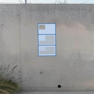 May include: A rectangular poster with a light blue border is attached to a concrete wall. The poster features a light blue top section with a small tan square, a middle section with horizontal tan stripes, and a bottom section with a tan star field.