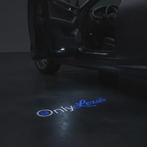 May include: A dark-colored vehicle with an open door projecting a bright blue light onto the ground. The light displays the text OnlyLexus in a stylized font, with the letter O featuring a circular icon inside, creating a glowing logo effect.