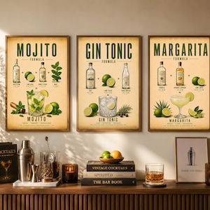 Peut inclure: Trois affiches encadrées de recettes de cocktails : Mojito, Gin Tonic et Margarita. Chaque affiche présente des illustrations des ingrédients et de la boisson finie. Les affiches sont exposées au-dessus d'un meuble en bois avec des accessoires et des livres de mixologie.