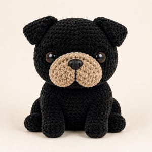 May include: A handmade black crochet pug dog with a tan muzzle and dark brown eyes. The plush toy is sitting upright with its legs extended. The pug has small, floppy ears and a black nose.
