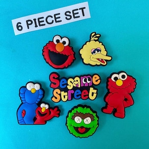 Puede incluir: Un juego de seis dijes de personajes de Barrio Sésamo. El juego incluye a Elmo, Big Bird, Monstruo de las Galletas y otros personajes. También se incluye el logotipo de Barrio Sésamo. Los dijes son de varios colores, incluyendo rojo, amarillo, azul y verde.