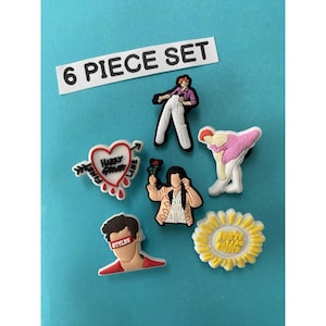 May include: A 6-piece set of decorative shoe charms. The charms feature various designs, including a heart with text, a sunflower, and figures in different poses. The text "6 PIECE SET" is displayed on a white rectangle.