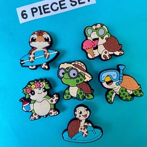 Puede incluir: Un conjunto de seis dijes con forma de tortuga de colores. Cada dije presenta un diseño de tortuga diferente, incluyendo una con una tabla de surf, otra con helado y otra con un esnórquel. El texto "6 PIECE SET" se muestra en la parte superior.