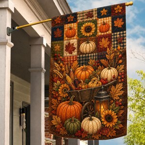 May include: A rectangular garden flag featuring a patchwork top section with pumpkins, sunflowers, and maple leaves. The lower portion displays a wooden wheelbarrow filled with pumpkins, corn, wheat, and sunflowers, alongside a lit lantern.