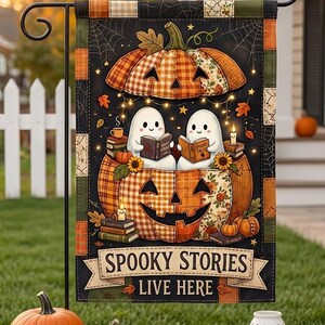 May include: A rectangular garden flag featuring two white ghosts reading books inside a large orange plaid pumpkin. The design includes spiderwebs, autumn leaves, and a banner at the bottom with the text SPOOKY STORIES LIVE HERE in black.