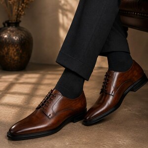 May include: A pair of polished brown leather oxford shoes featuring a smooth finish, dark brown laces, and a black sole. The shoes are worn with black socks and black trousers, showcasing a classic silhouette with a rounded toe and stitching.