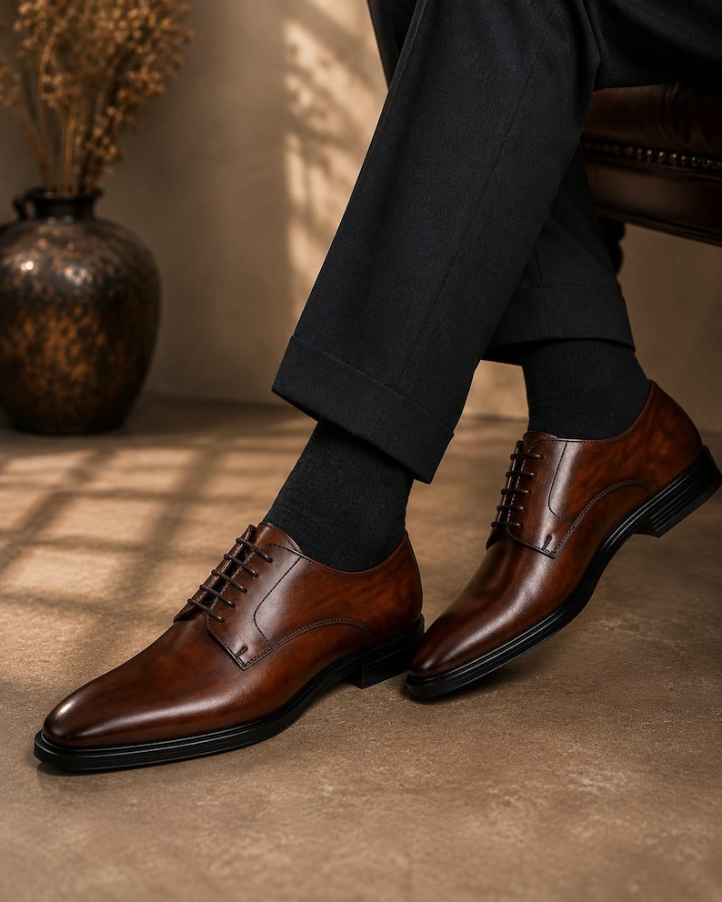 May include: A pair of polished brown leather oxford shoes featuring a smooth finish, dark brown laces, and a black sole. The shoes are worn with black socks and black trousers, showcasing a classic silhouette with a rounded toe and stitching.
