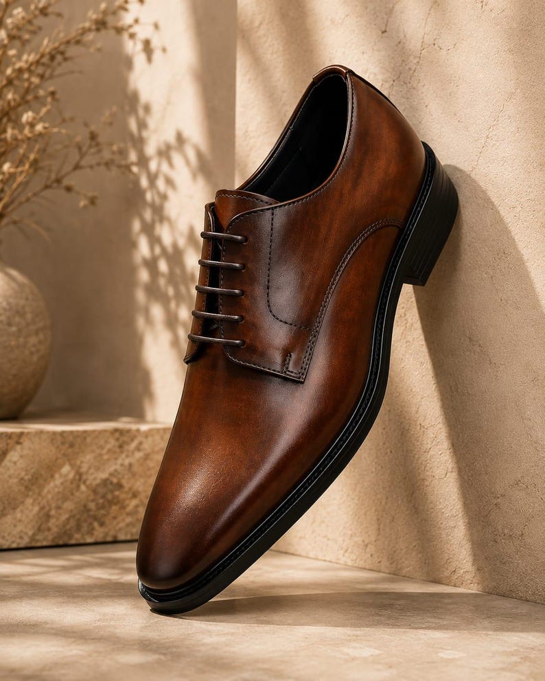 May include: A polished brown leather oxford shoe featuring a smooth, burnished finish, a classic lace-up closure with dark brown laces, a rounded toe, and a solid black sole. The shoe is constructed with visible stitching along the side panels.