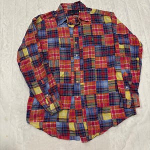 Può includere: Una camicia a maniche lunghe con bottoni caratterizzata da un motivo a quadri patchwork multicolore nelle tonalità del rosso, blu e giallo. La camicia presenta un colletto standard, un'abbottonatura frontale e un piccolo logo ricamato sul petto.