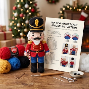 May include: A crocheted nutcracker doll with a black hat, red coat, and blue pants, standing next to a printed pattern titled NO-SEW NUTCRACKER AMIGURUMI PATTERN. The scene includes balls of red, blue, yellow, and black yarn, a 3.5mm crochet hook, a needle, and small black eyes.