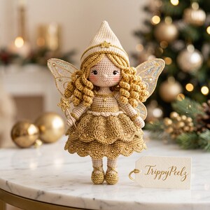 May include: A crocheted fairy doll with curly golden hair, wearing a pointed hat and a layered gold dress. The doll has iridescent wings, holds a gold star wand, and stands next to a white tag with the gold text TrippyPeelz printed on it.