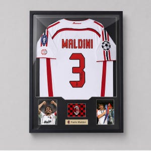 Puede incluir: Un marco con recuerdos deportivos que presenta una camiseta blanca del AC Milan con el nombre MALDINI y el número 3 en la espalda. La exhibición incluye dos fotografías de Paolo Maldini, un escudo del equipo y una placa en un marco negro.