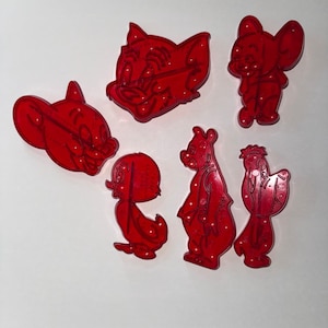 May include: A set of six red translucent plastic cookie cutters featuring various cartoon character shapes, including two cat heads, a mouse, a small bird, a tall bear-like figure, and a stylized character with a tuft of hair on its head.