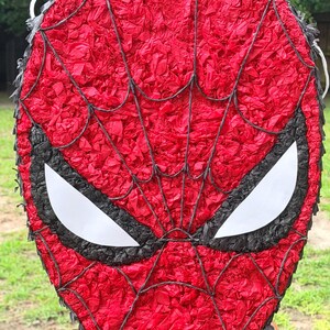 May include: A red Spider-Man pi&ntilde;ata with a black web design and white eye shapes. The pi&ntilde;ata is made of red tissue paper and is designed to resemble the superhero's mask. Great for a birthday party.