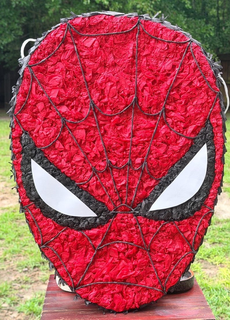 May include: A red Spider-Man pi&ntilde;ata with a black web design and white eye shapes. The pi&ntilde;ata is made of red tissue paper and is designed to resemble the superhero's mask. Great for a birthday party.