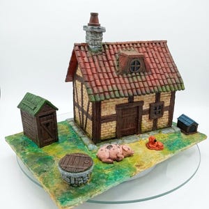May include: A miniature diorama featuring a timber-framed cottage with a red tiled roof and chimney. The scene includes a small wooden outhouse, a stone well, a pink pig, a small orange dog, and a blue doghouse, all set on a green base.