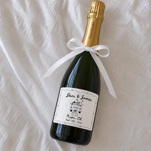 Puede incluir: Una botella de champán Veuve Clicquot con cuello de papel de aluminio dorado y una cinta blanca atada en un lazo. La etiqueta personalizada presenta una ilustración en blanco y negro de un coche con el texto Dani & James, Napa, CA, y Sept 12th, 2026.