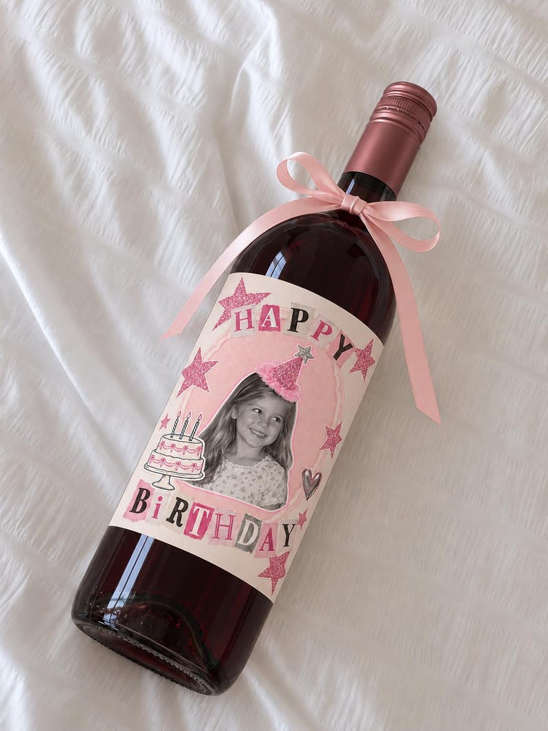 Puede incluir: Una botella de vino de cristal con tap&oacute;n de rosca rosa y un lazo rosa claro atado al cuello. La etiqueta muestra la foto de un ni&ntilde;o con un gorro de fiesta, un pastel de cumplea&ntilde;os, estrellas rosas brillantes y el texto HAPPY BIRTHDAY.
