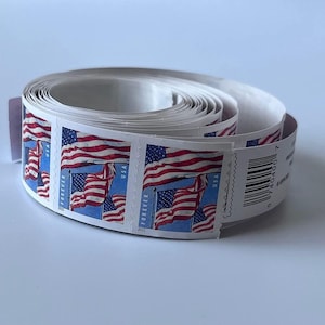 May include: A roll of adhesive postage stamps featuring a graphic of the American flag waving against a blue sky. Each stamp includes the text FOREVER, USA, and 2022. The roll includes a white paper backing and a barcode on the end of the strip.