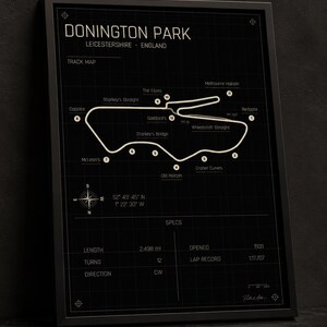 Op de afbeelding: Ingelijste print van het Donington Park circuit in Leicestershire, Engeland. De circuitkaart is wit op een zwarte achtergrond, met gelabelde bochten en een windroos. De print bevat circuitspecificaties.